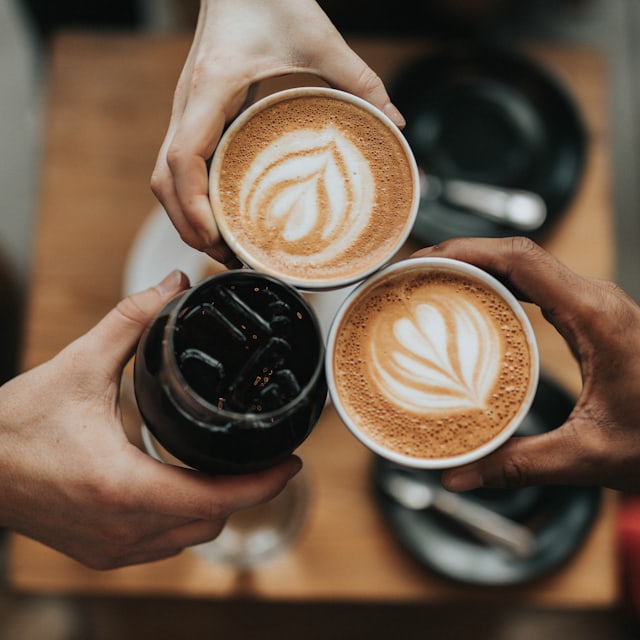 Three people holding coffee cups with latte art together over a café table