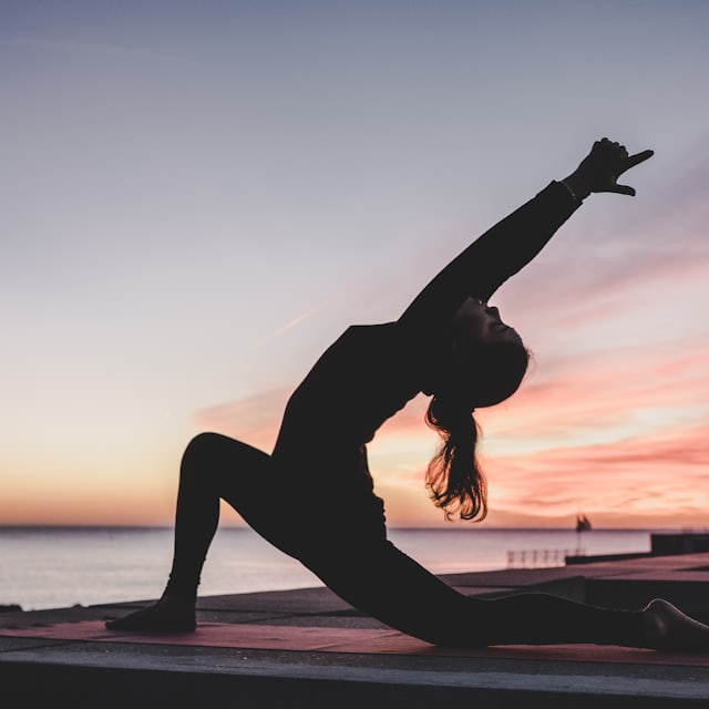 Person in a yoga lunge pose silhouetted against a sunset sky